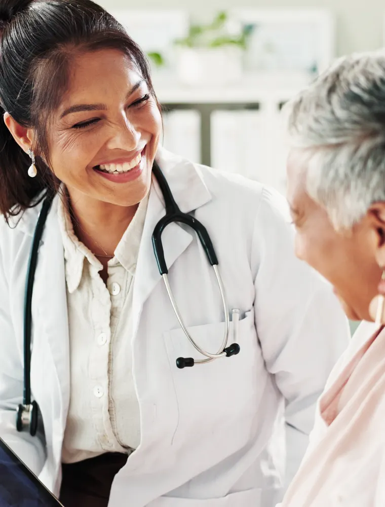 A clinician talks with a smiling older patient in a bright exam room